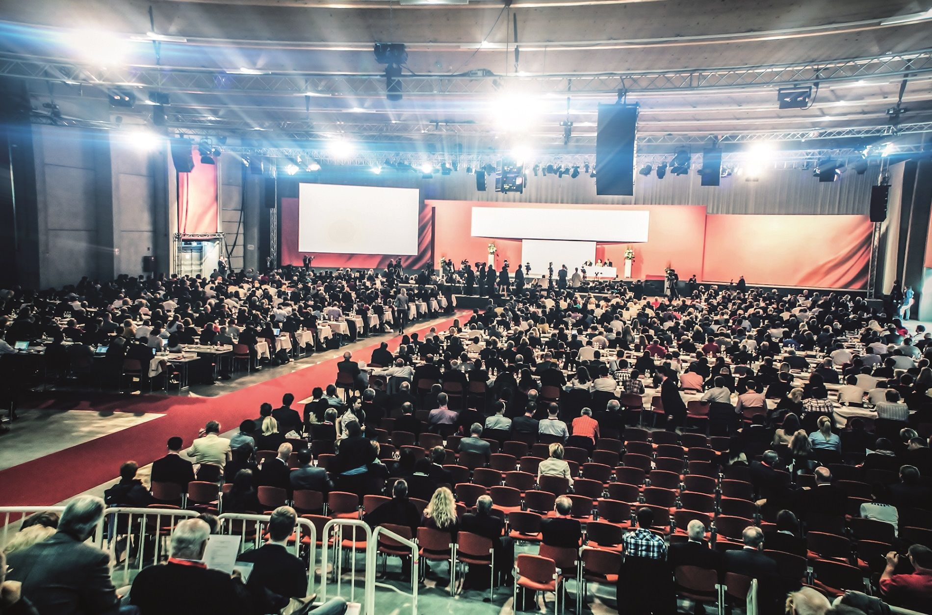 Nagy kongresszusi terem sok résztvevővel, színpaddal és vetítővászonnal.