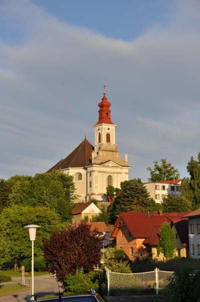 Zarándoktemplom egy dombon, vörös tetővel és fákkal az előtérben.