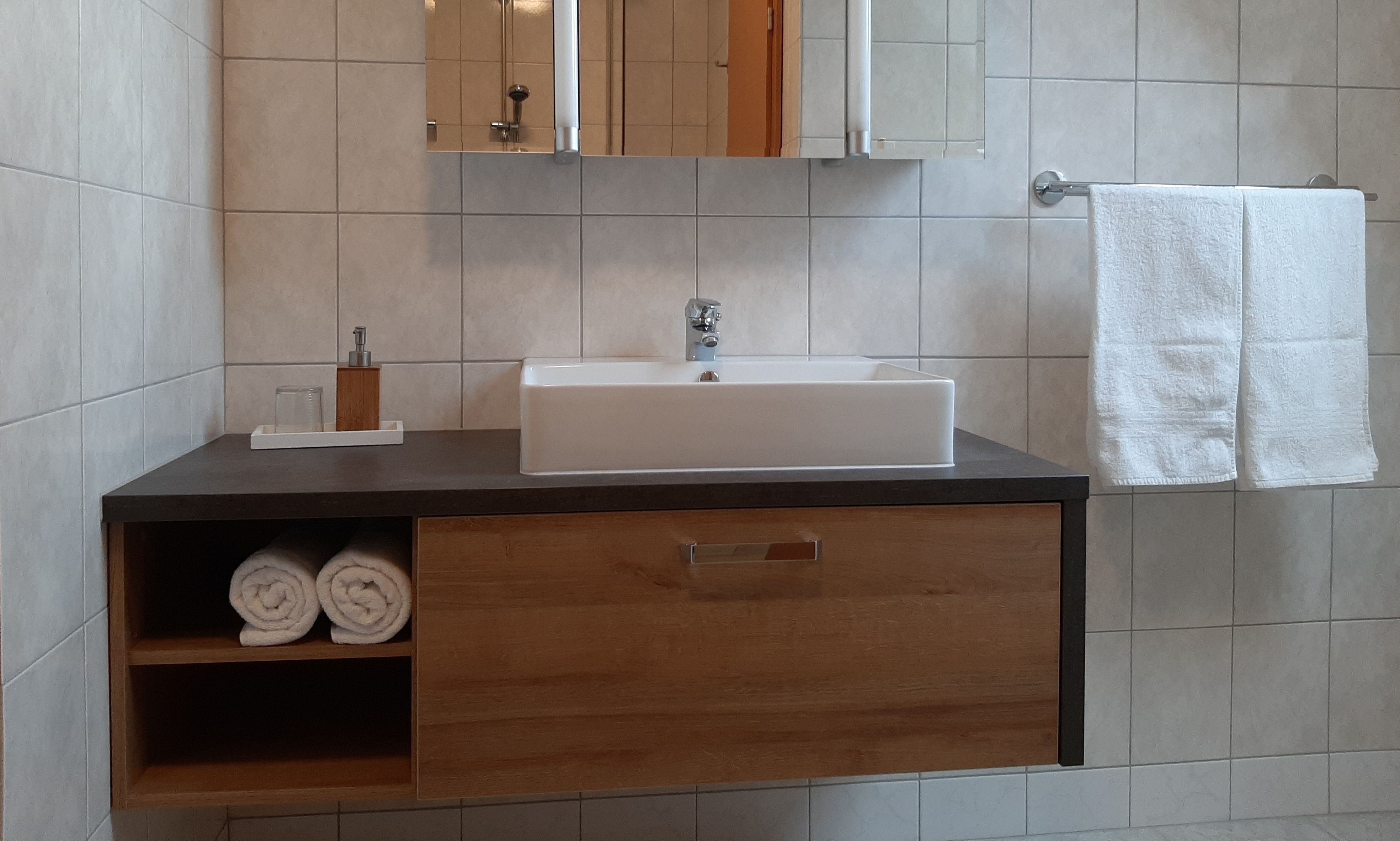 Modern fürdőszoba mosdóval, törölközővel és tükörrel.