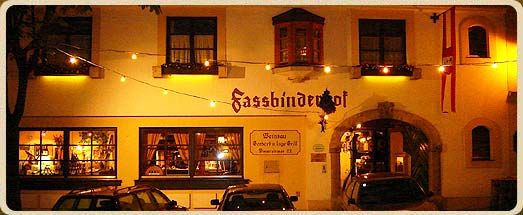 Éjszakai felvétel egy "Fassbinderhof" feliratú épületről, tündérfényekkel megvilágítva.