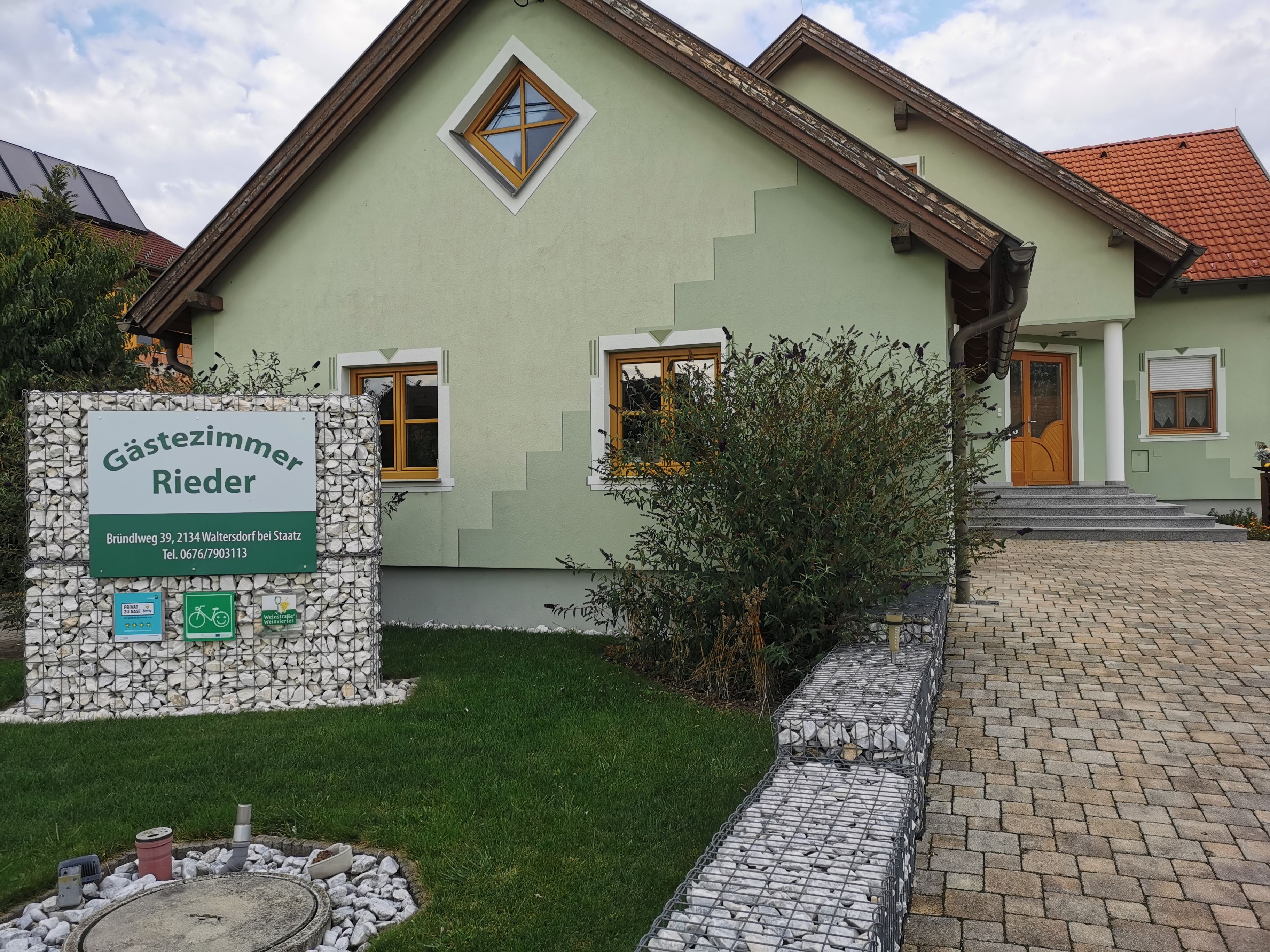 Zöld ház "Gästezimmer Rieder" felirattal a teraszon.