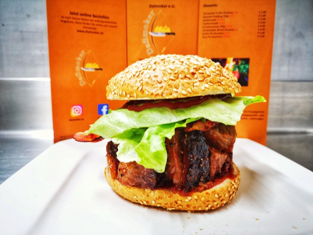 Egy burger salátával és hússal egy fehér tányéron, egy narancssárga színű étlap előtt.