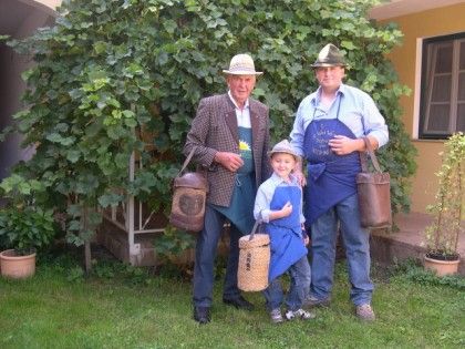 Három generációnyi hagyományos öltözetű férfi kosarakkal a kertben.