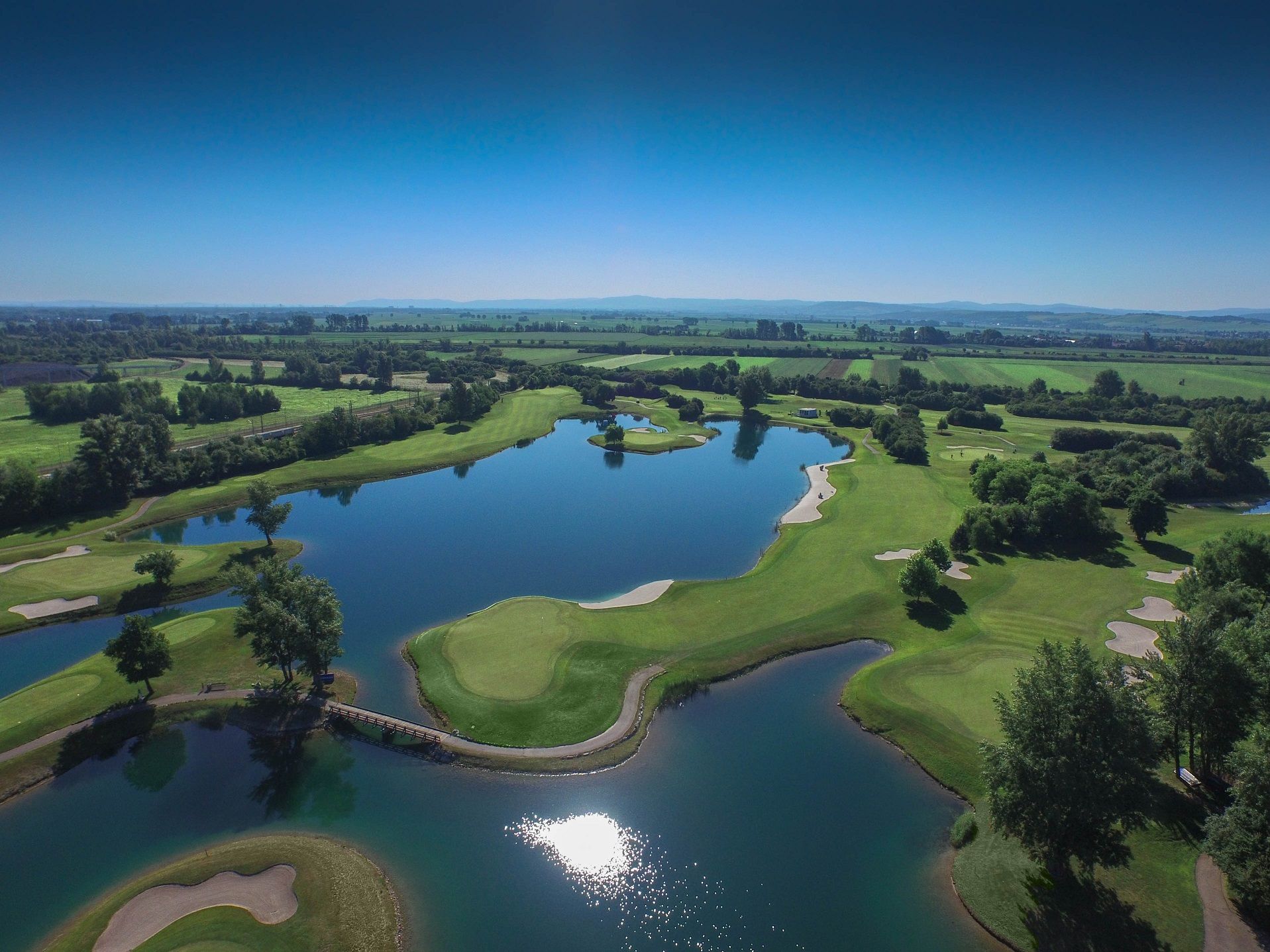 Légi felvétel egy golfpályáról, vízakadályokkal és zöld pályákkal.