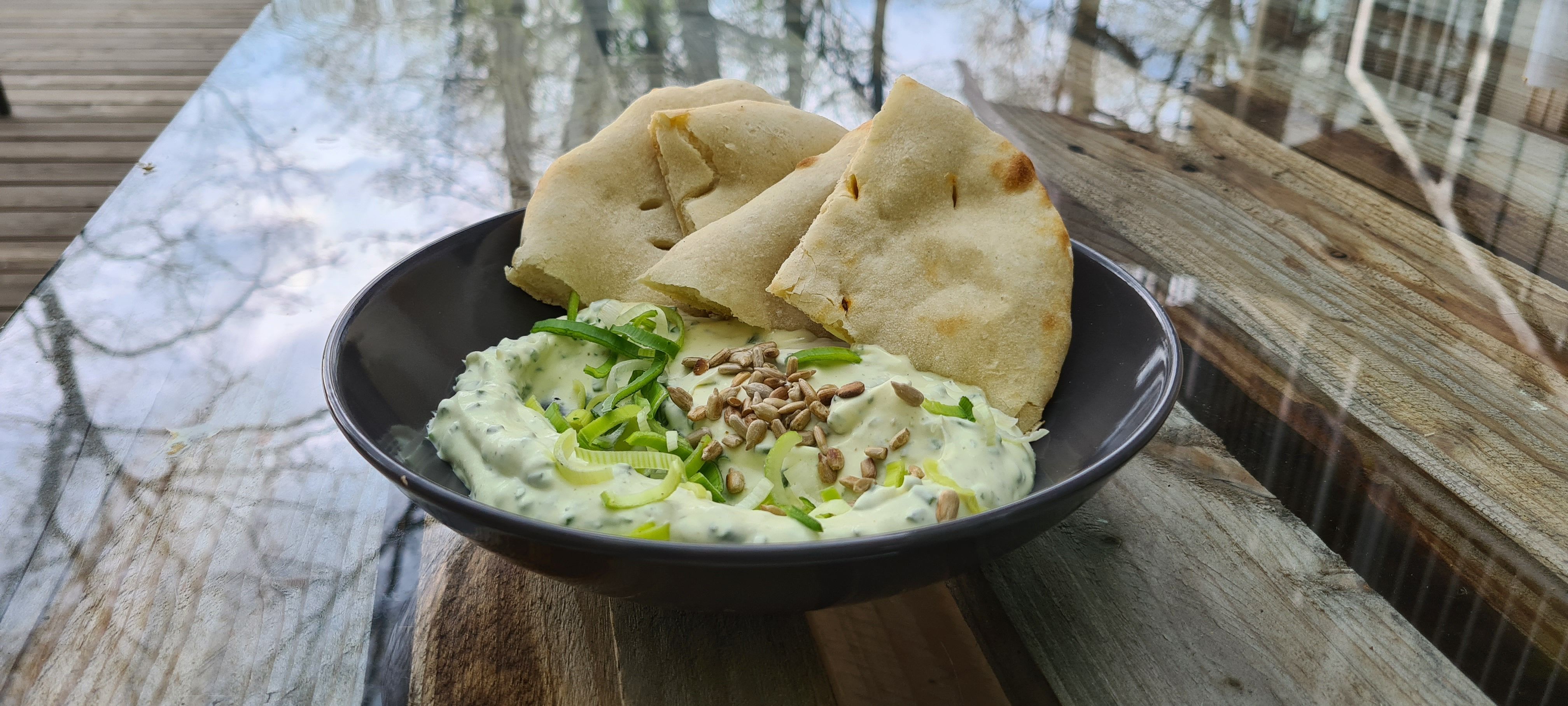 Fekete tál mártással és kenyérdarabokkal egy faasztalon.