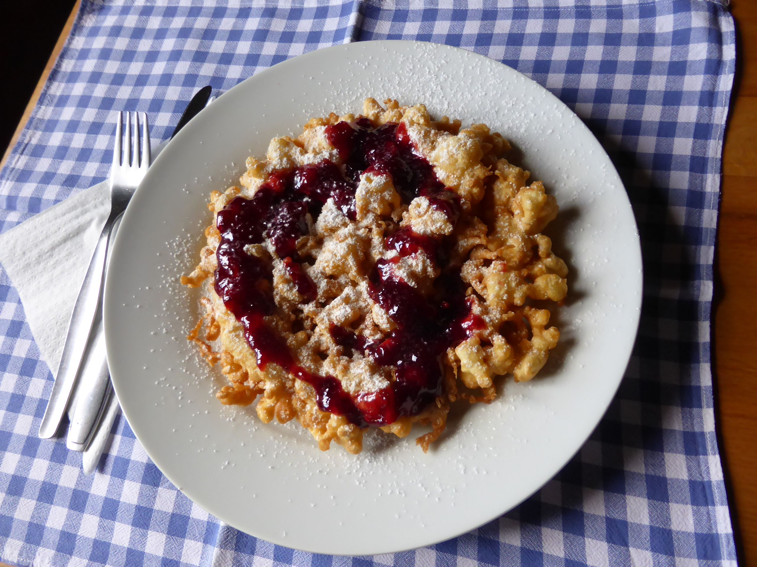 Egy tányér Kaiserschmarrn és piros gyümölcskocsonya kék-fehér kockás terítőn.