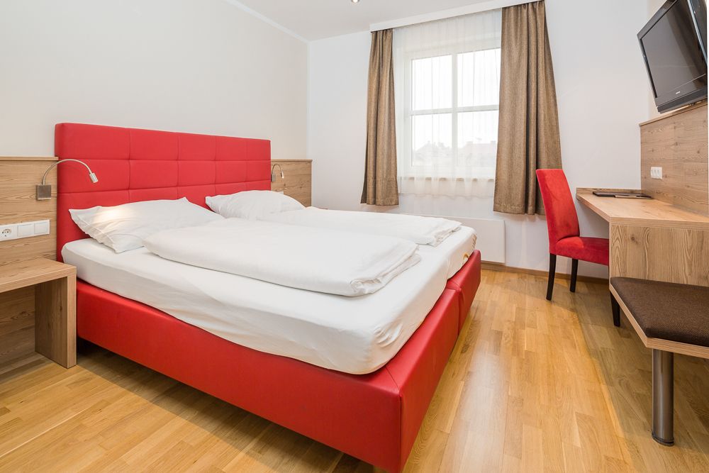 Modern szállodai szoba piros ággyal és íróasztallal.