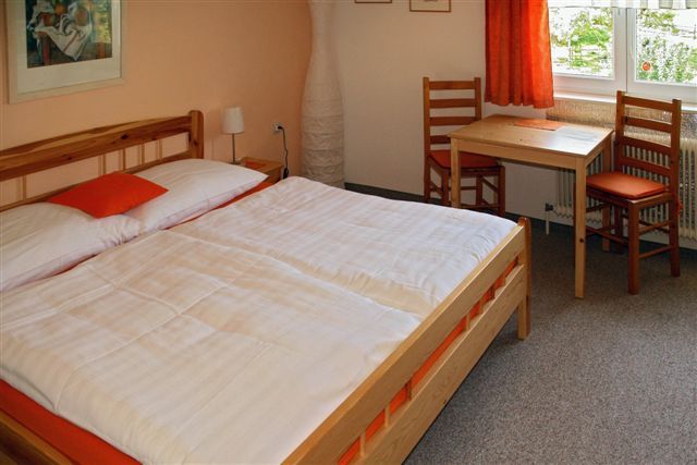 Hangulatos vendégszoba franciaággyal, fabútorokkal és egy kis asztallal az ablak mellett.