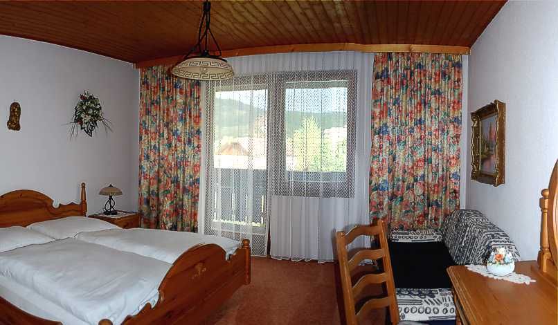 Hangulatos hotelszoba fabútorokkal, franciaággyal, erkéllyel és színes függönyökkel.