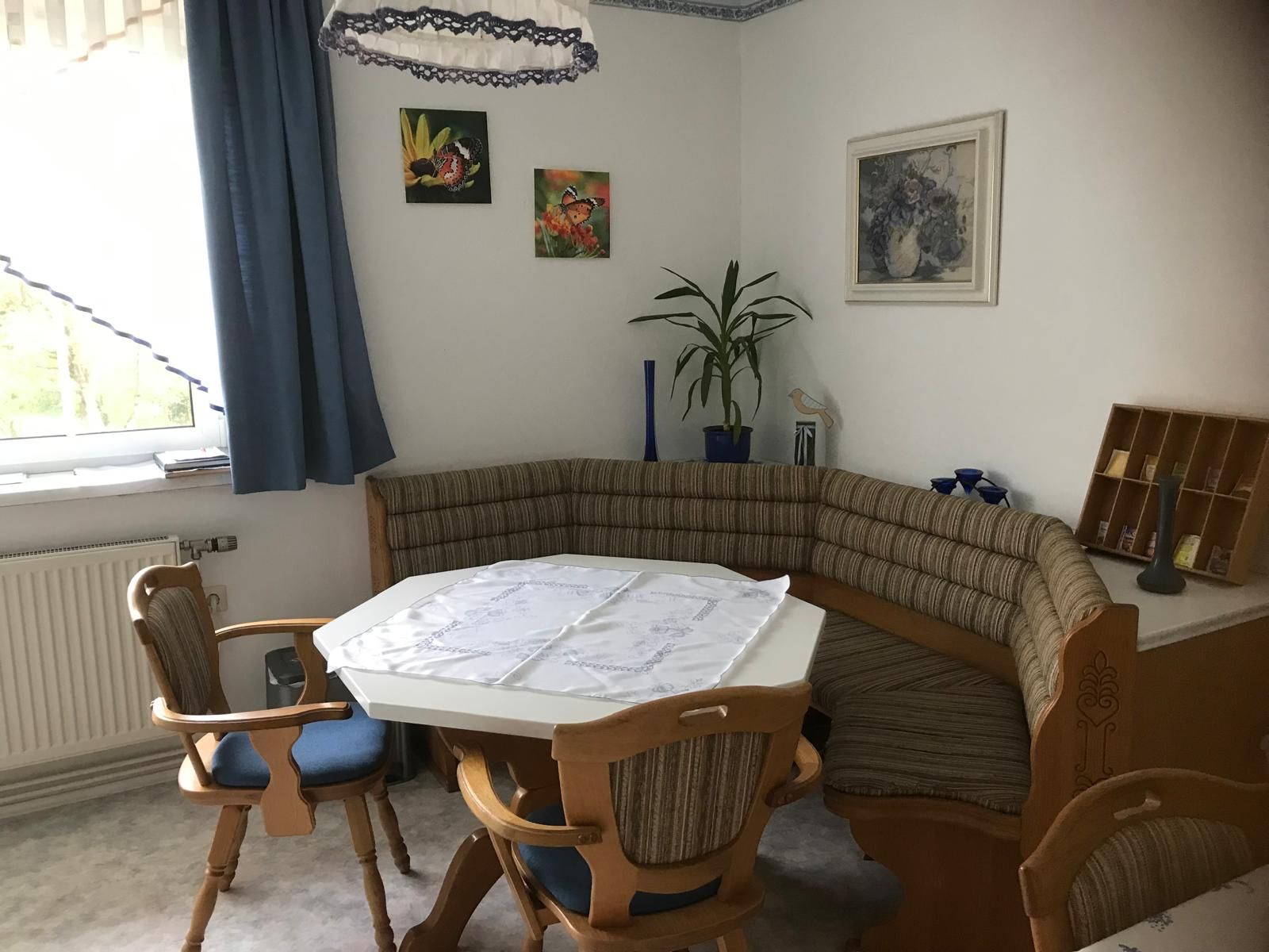Sarokpad egy konyhában asztallal és székekkel, növényekkel és képekkel díszített falon.