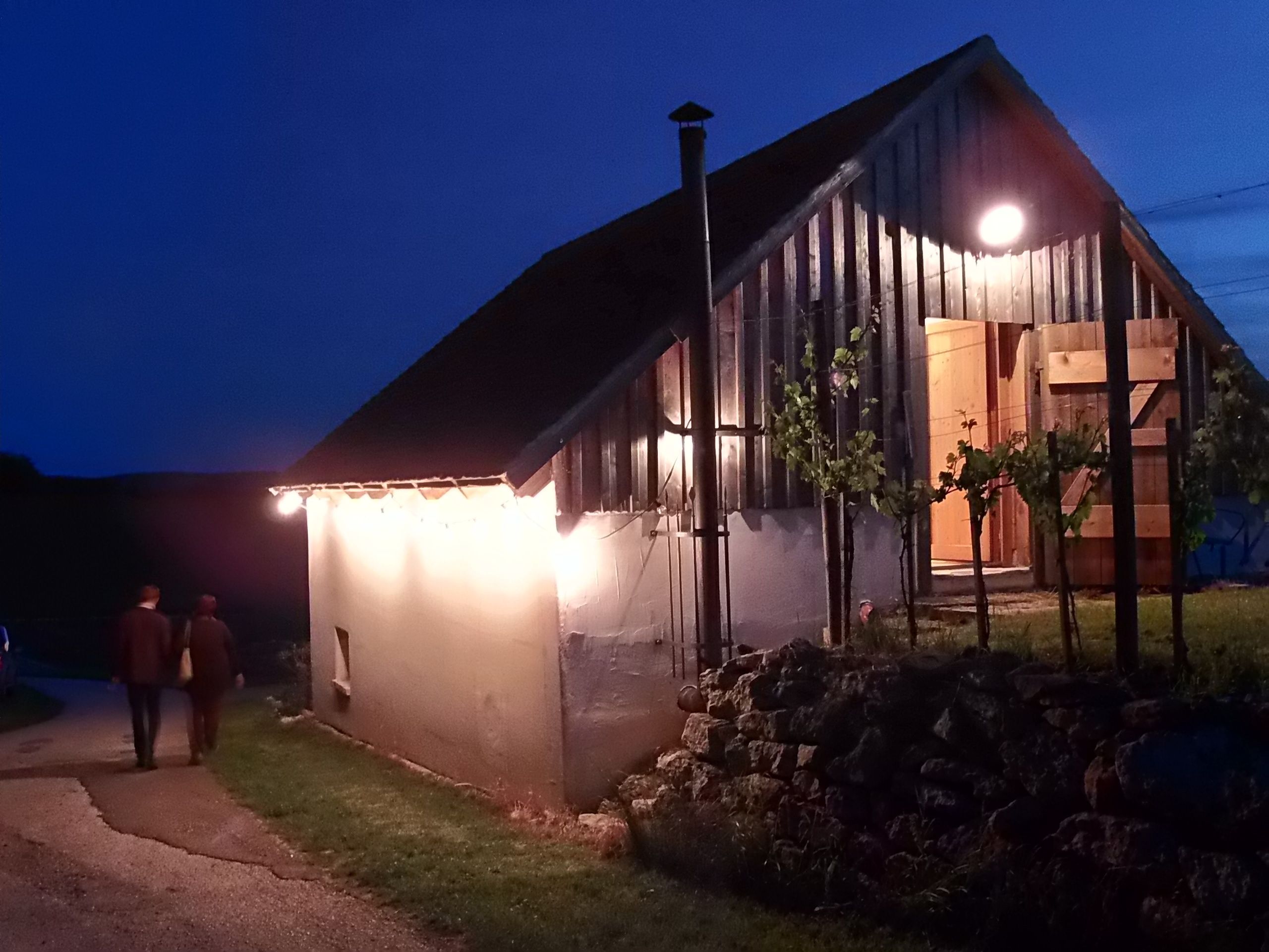 Megvilágított borospince épület éjszaka két emberrel egy ösvényen.