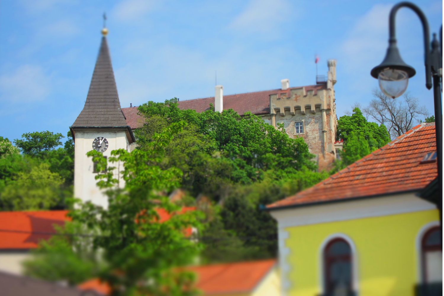 Templomtorony és kastély a fák mögött, kék ég.