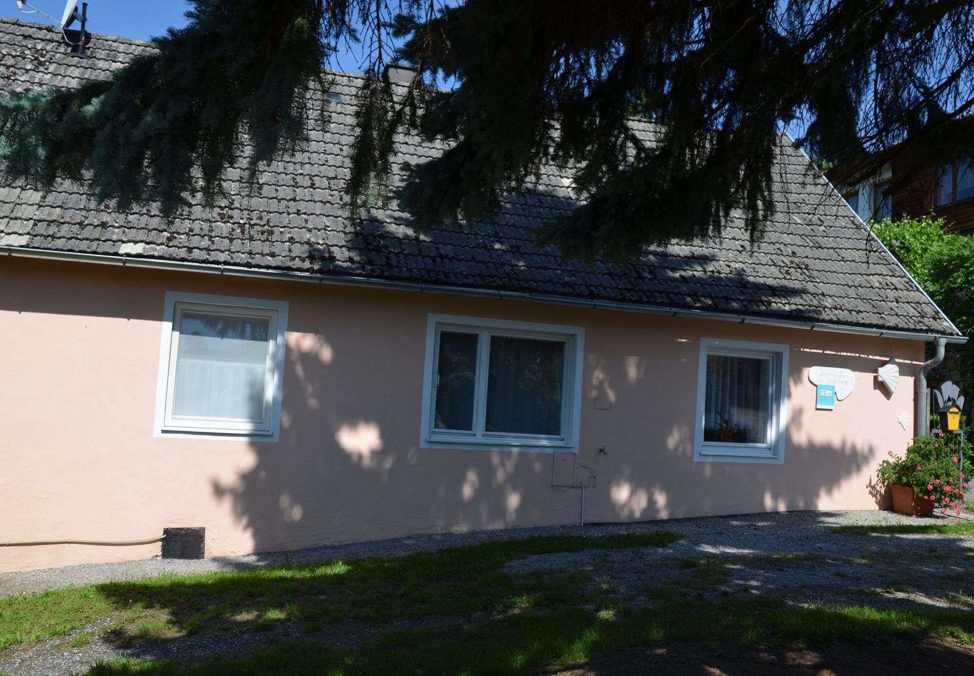 Egy kis, rózsaszínű nyaraló, az előtérben árnyas fákkal.