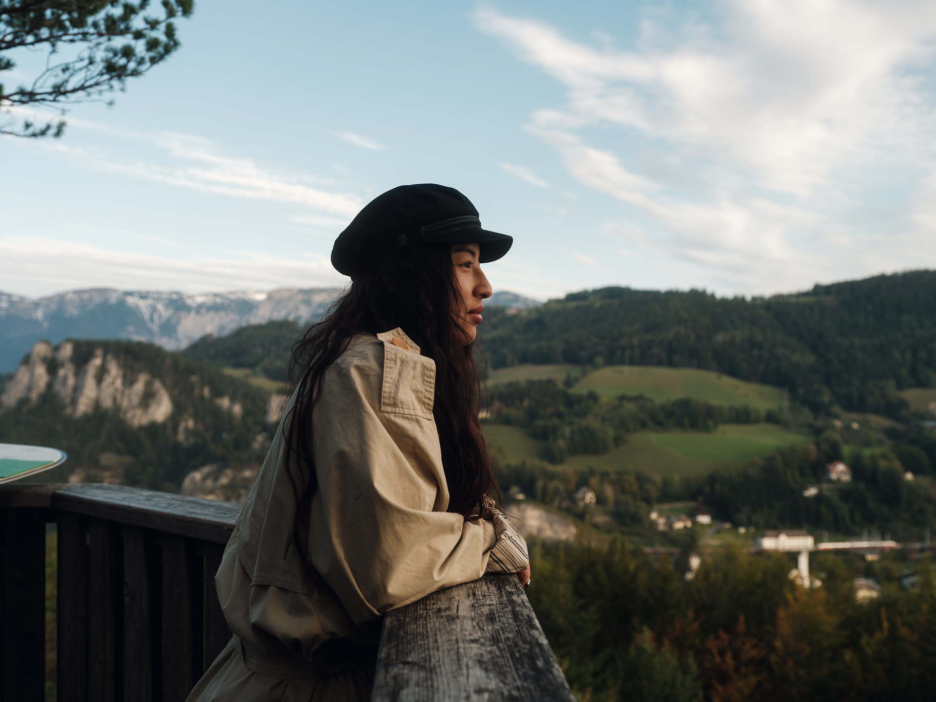 In der sanften Abenddämmerung genießt eine Frau die atemberaubende Aussicht auf die umliegenden Berge und Täler. Die frische Bergluft und die malerische Landschaft laden dazu ein, die Seele baumeln zu lassen und die Schönheit der Natur zu erleben.
