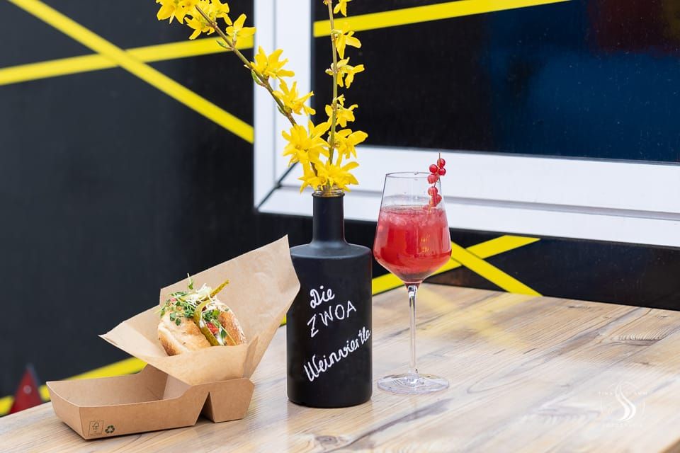 Egy ital és egy szendvics az asztalon, egy váza sárga virággal.