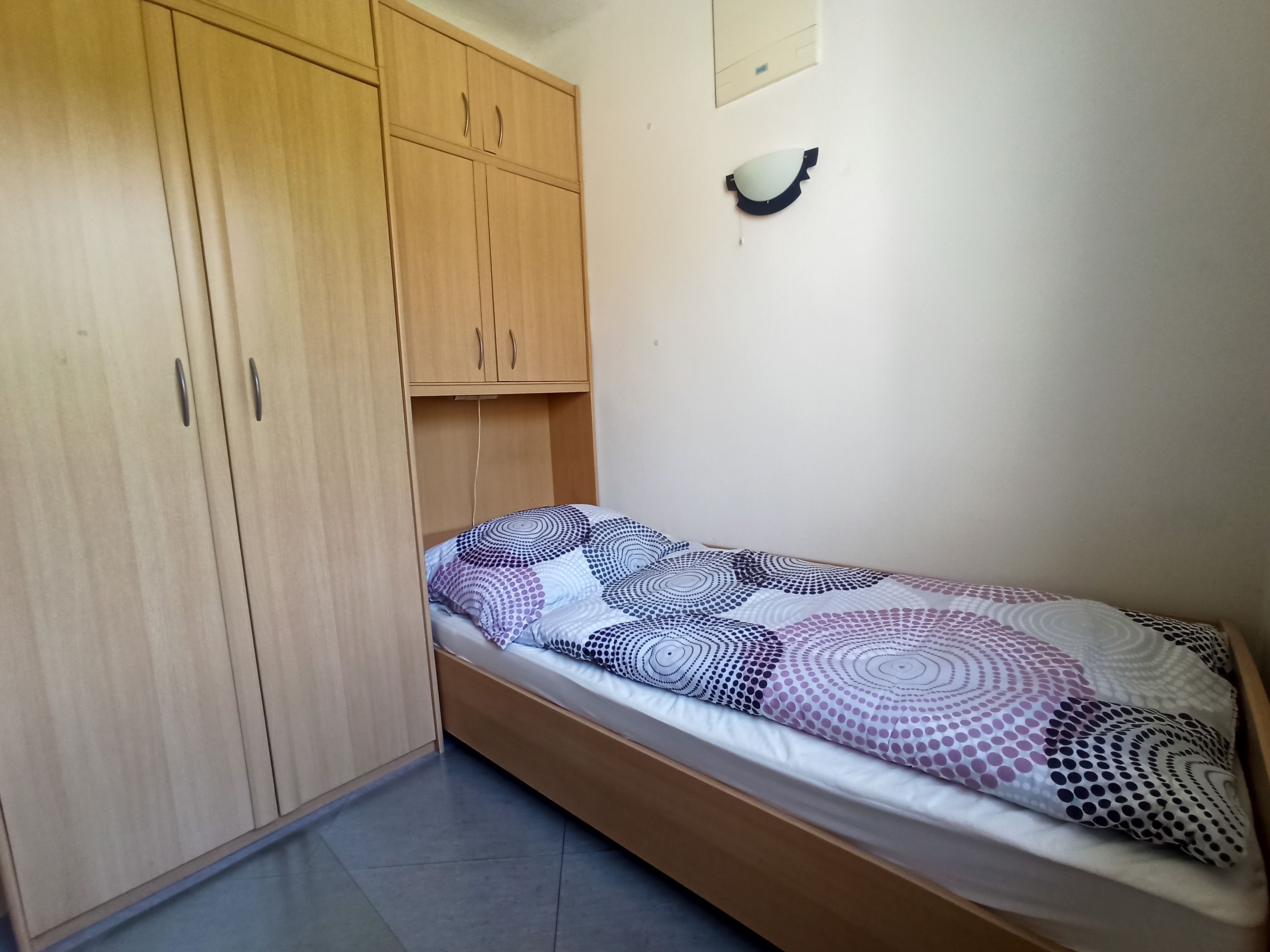 Egy egyszerű hálószoba egy egyszemélyes ággyal és egy nagy fa szekrénnyel.