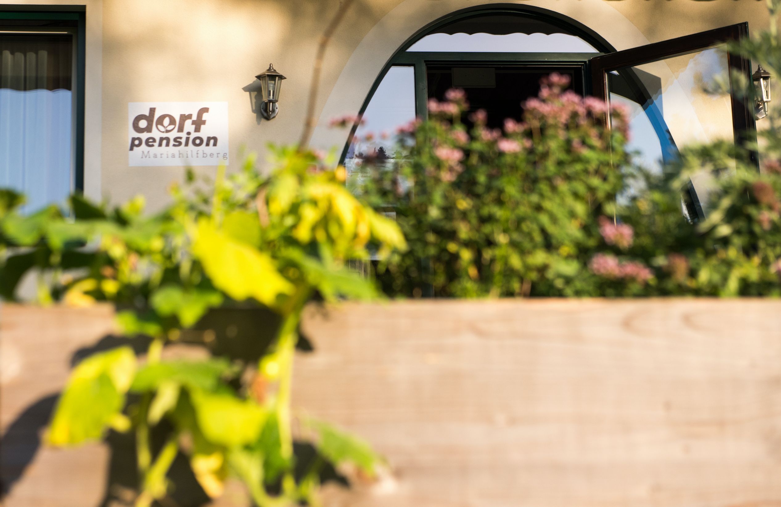 A Mariahilfberg falusi vendégház bejárata, előtérben növényekkel.