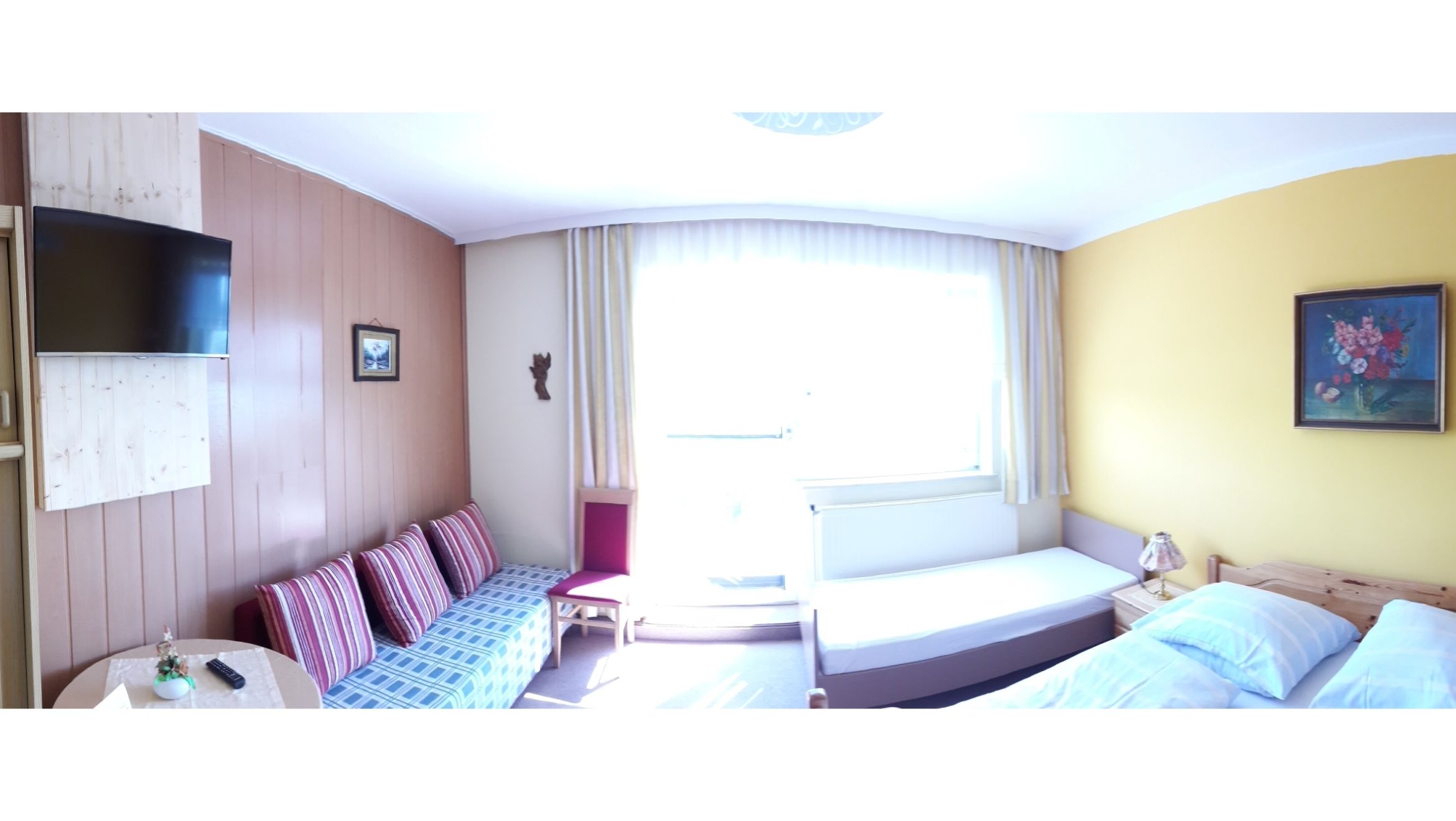 Világos vendégszoba kanapéval, ággyal, TV-vel és festménnyel a falon.