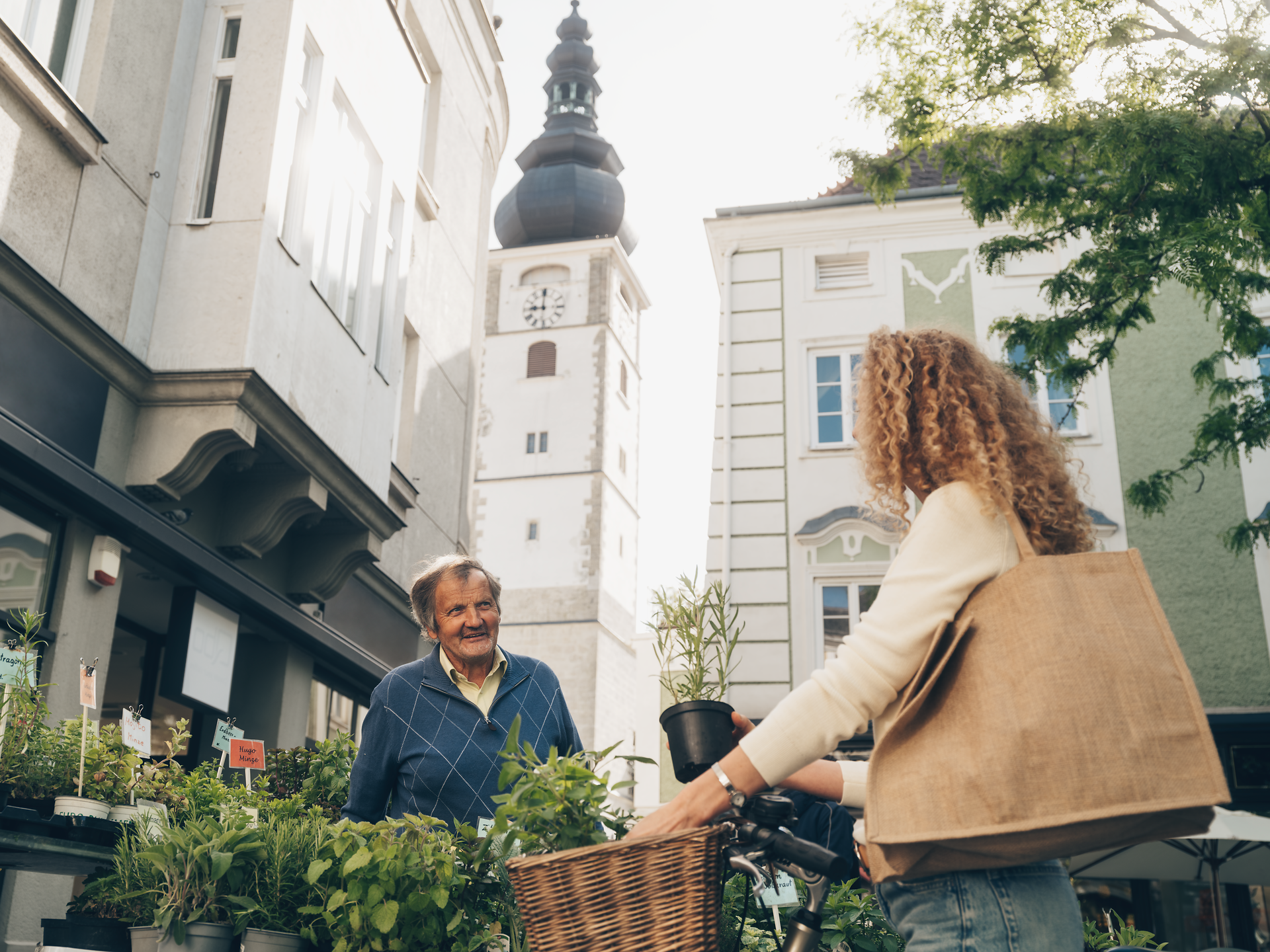 Ein charmantes Treffen zwischen einem freundlichen Verkäufer und einer interessierten Kundin auf dem Wochenmarkt. Die bunten Pflanzen und frischen Kräuter schaffen eine einladende Atmosphäre, die die Sinne anregt und die Vorfreude auf kulinarische Genüsse weckt.