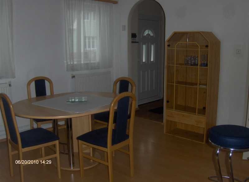 Étkezőhelyiség kerek asztallal, négy székkel és egy fából készült polccal egy világos szobában.