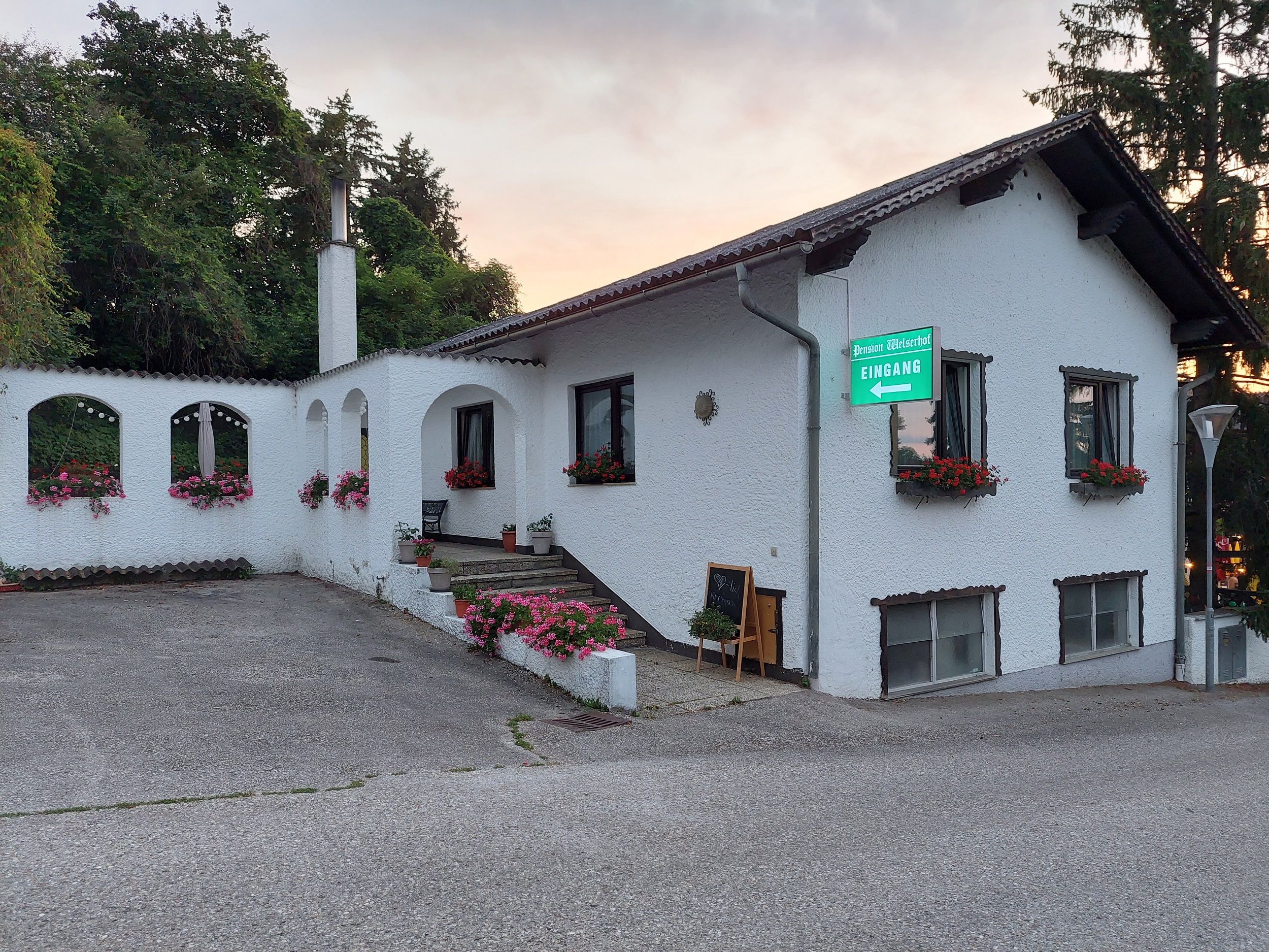 Egy fehér épület külső nézete virágokkal és a "Pension Welserhof Eingang" felirattal.