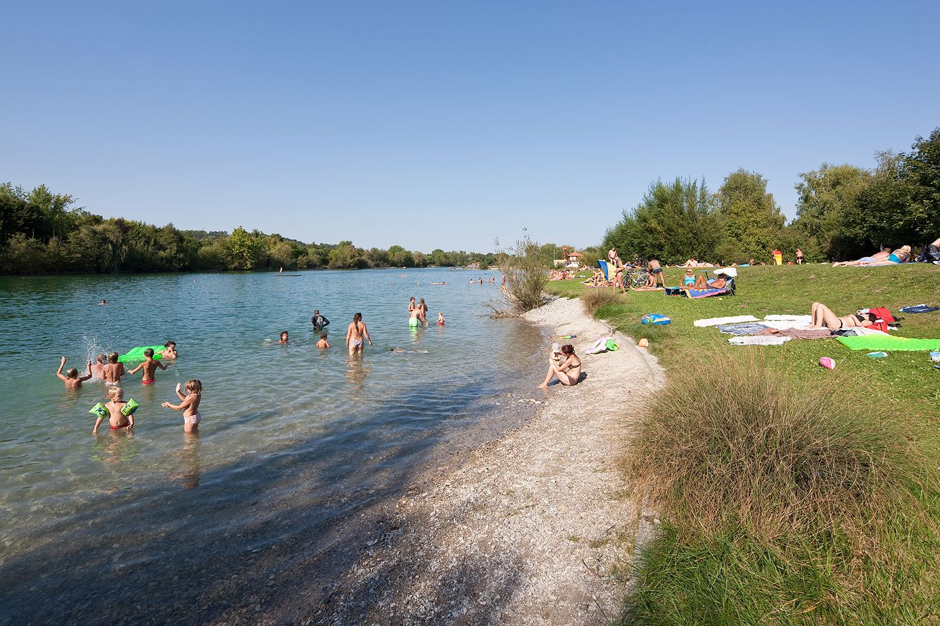 Emberek úsznak és pihennek a Ratzersdorfi tónál egy napsütéses napon.