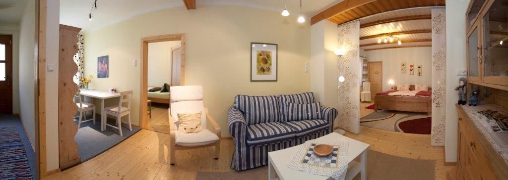 Panoráma egy hangulatos nappaliról, kanapéval, étkezőasztallal és hálószobával a háttérben.