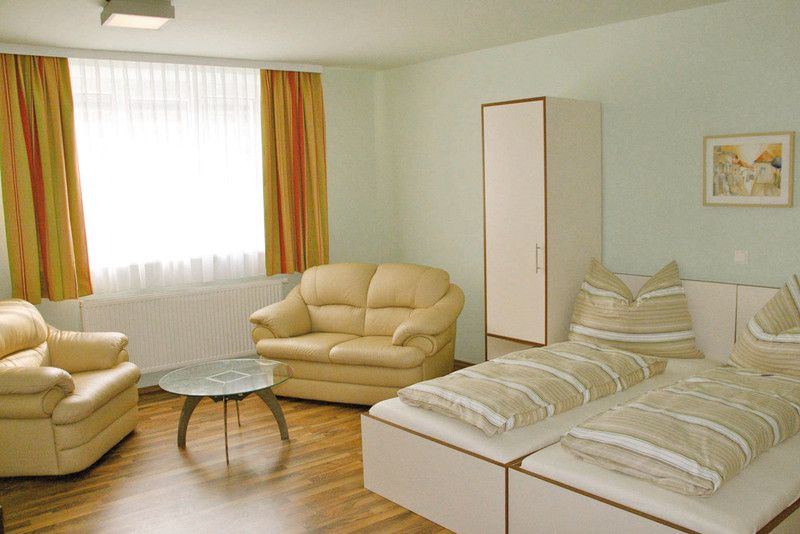 Világos szoba két ággyal, kanapéval, asztallal és szekrénnyel.
