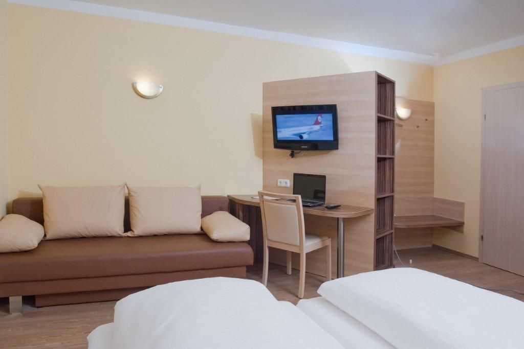 Hotelszoba kanapéval, íróasztallal, televízióval és ággyal.