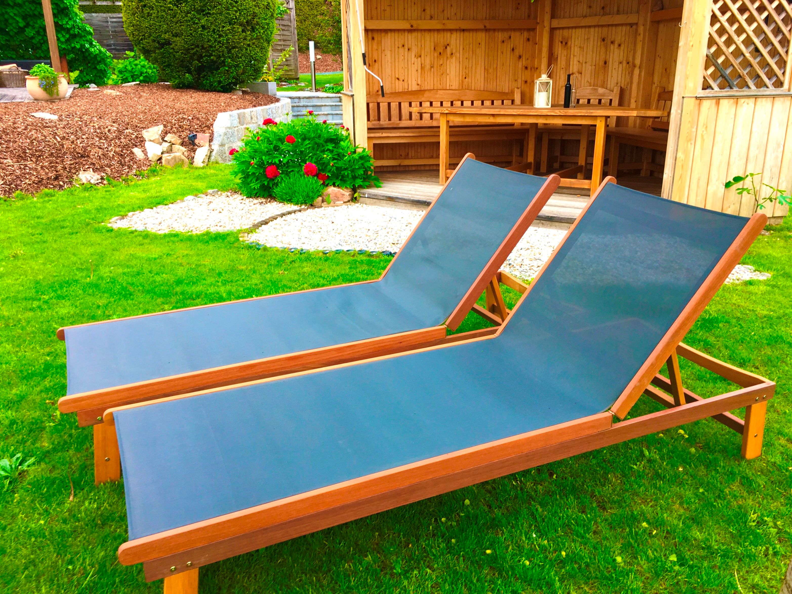 Két kék nyugágy a zöld gyepen egy faház előtt a kertben.