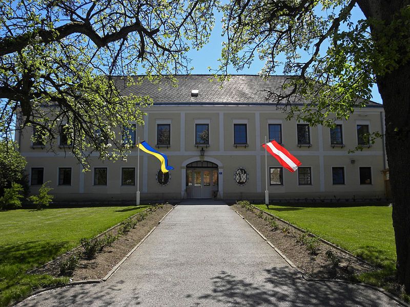 Hochwolkersdorfi kastély két zászlóval, fákkal és pázsittal körülvéve.