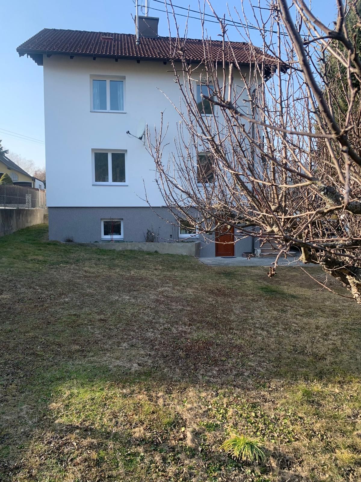 Egy fehér ház külső nézete piros tetővel és kerttel.