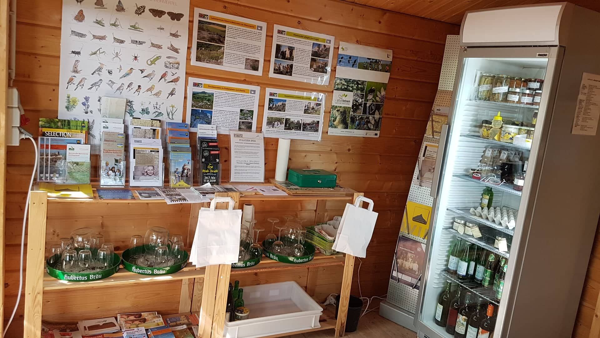 Belső nézet egy kis elárusító standról, információs anyaggal és hűtőszekrénnyel.