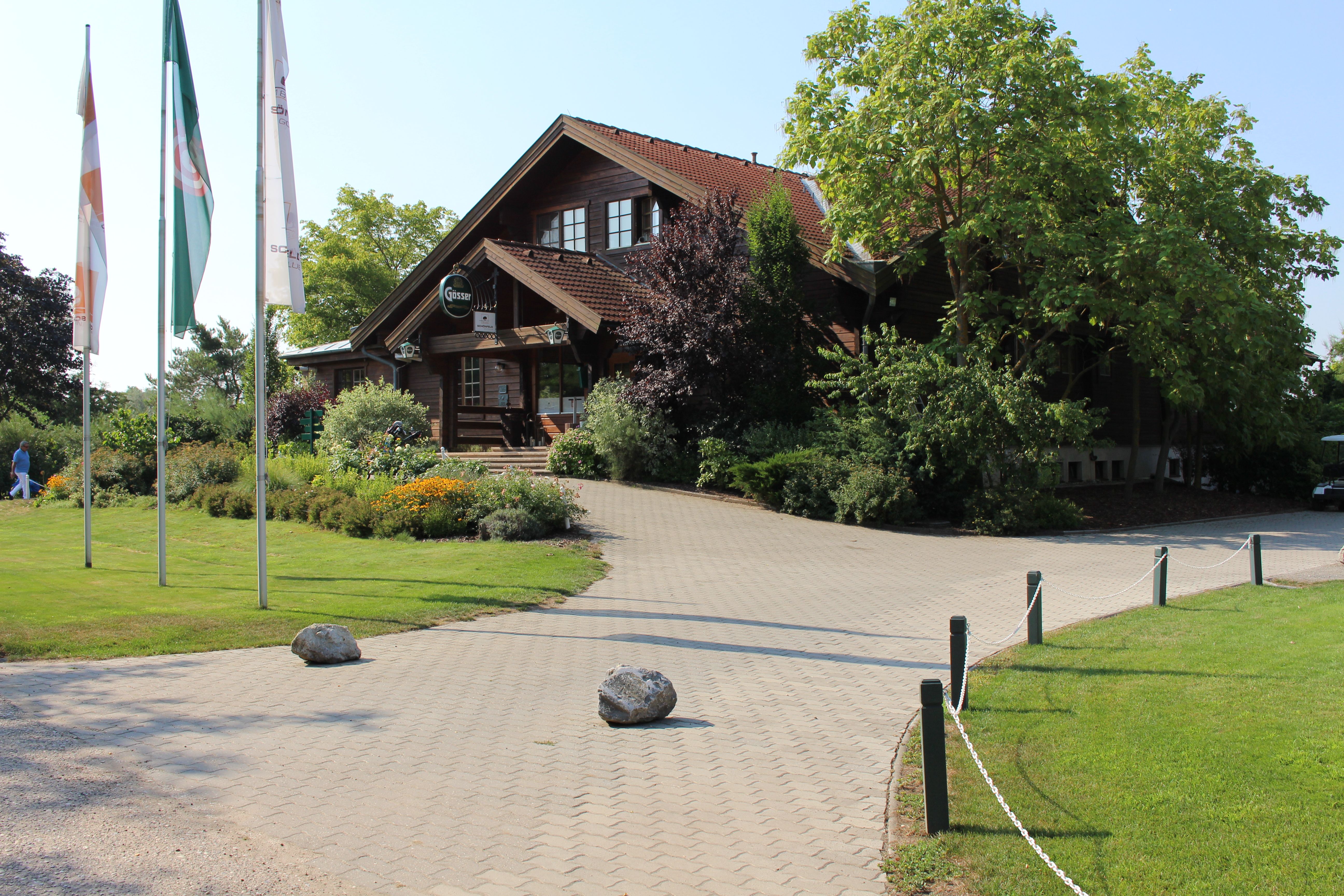 Egy golfklub bejárata faépülettel és zászlókkal.