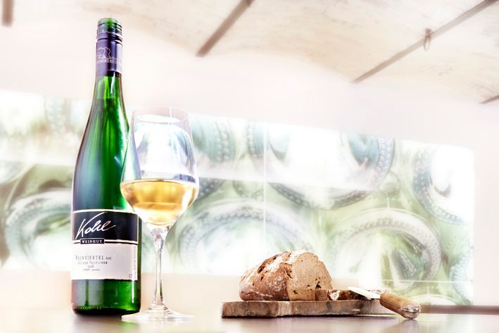 Egy üveg fehérbor, egy teli borospohár és egy kenyér az asztalon.