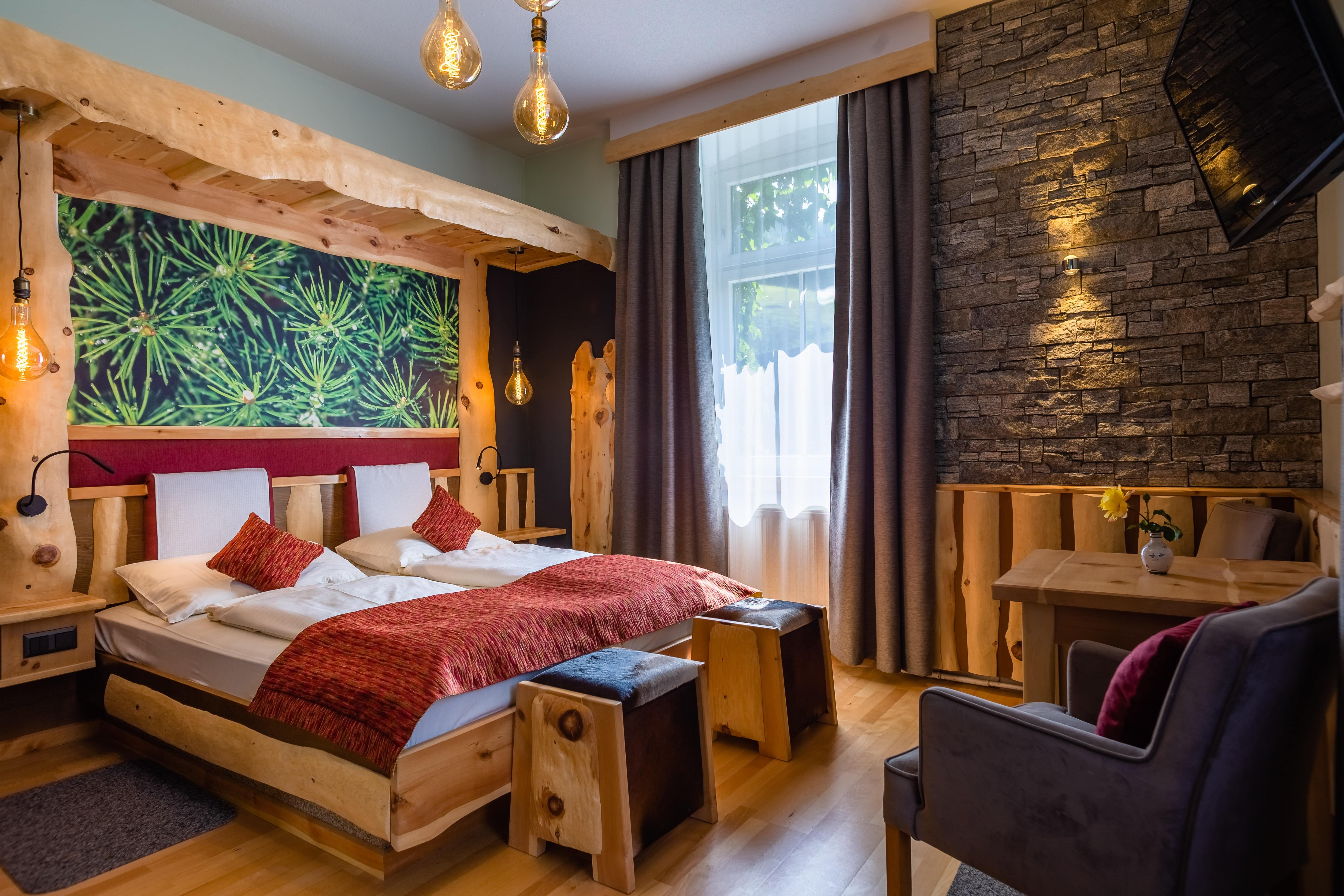 Hangulatos hotelszoba fabútorokkal, kőfallal és nagy ablakkal.