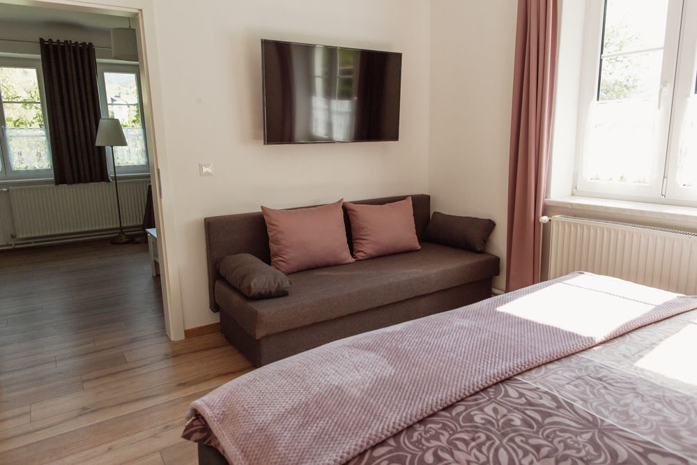 Modern nappali kanapéval, síkképernyős TV-vel és rózsaszín függönyös ablakkal.