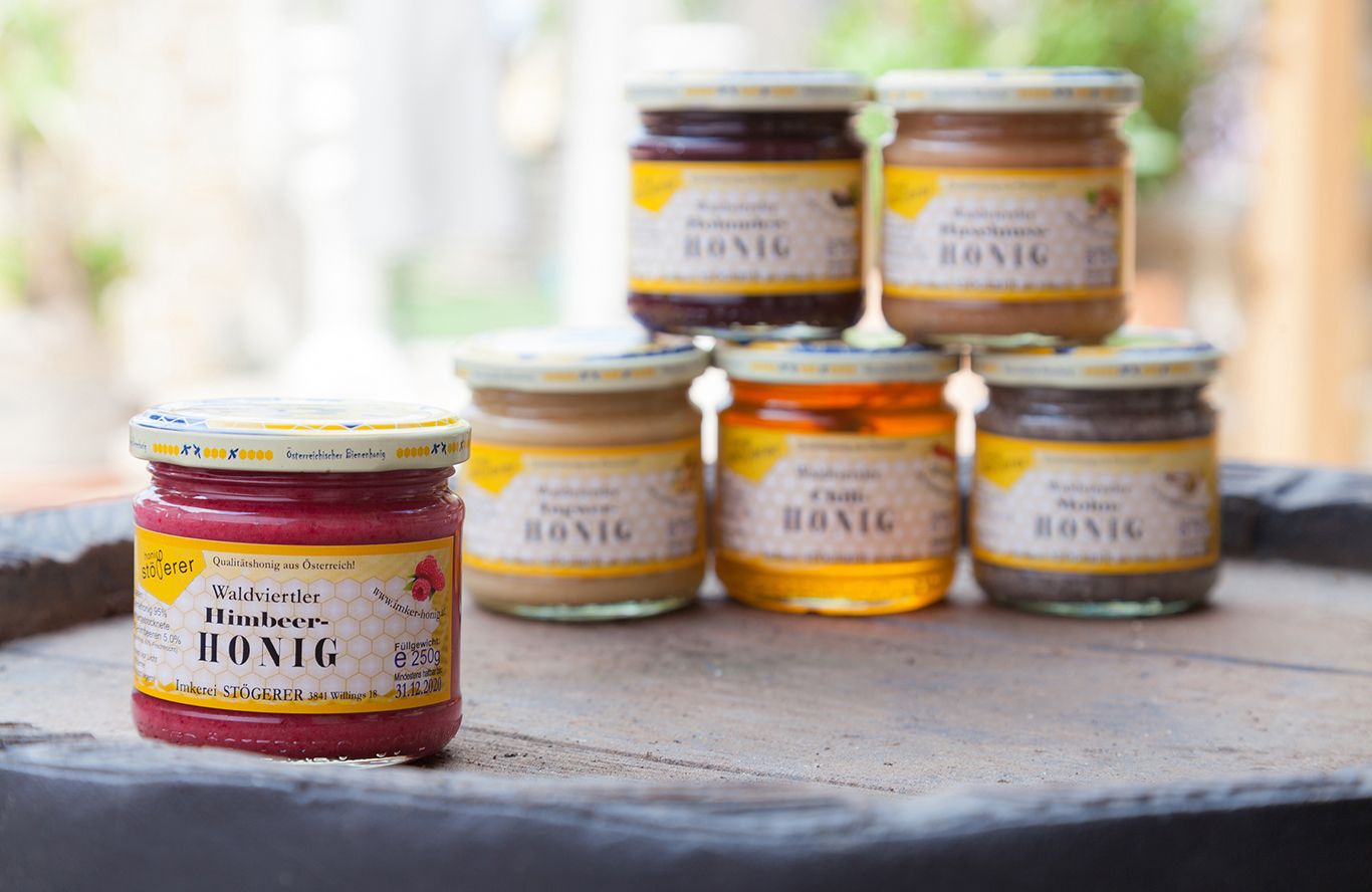 Különböző mézesüvegek egy asztalon, előtérben málnaméz.