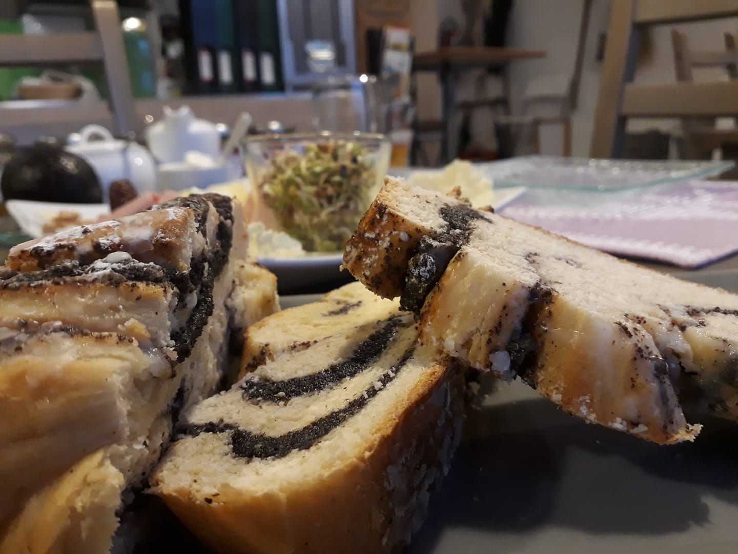 Mákos sütemény közelképe egy reggelizőasztalon, elmosódott háttérrel.