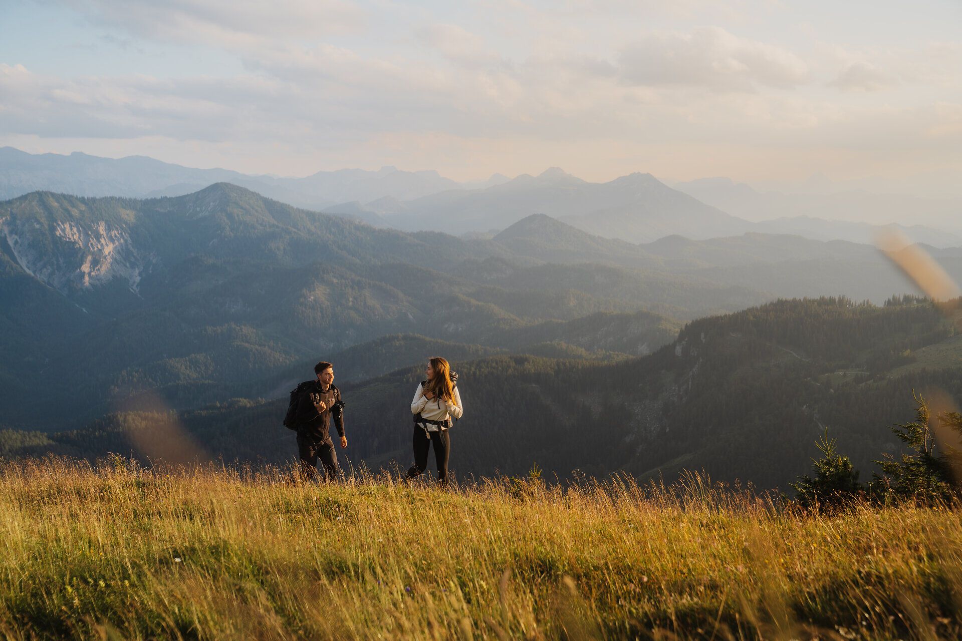 In der sanften Abenddämmerung wandern zwei Abenteurer über die blühenden Wiesen, umgeben von majestätischen Bergen. Die frische Luft und die atemberaubende Aussicht laden dazu ein, die Schönheit der Natur in vollen Zügen zu genießen.