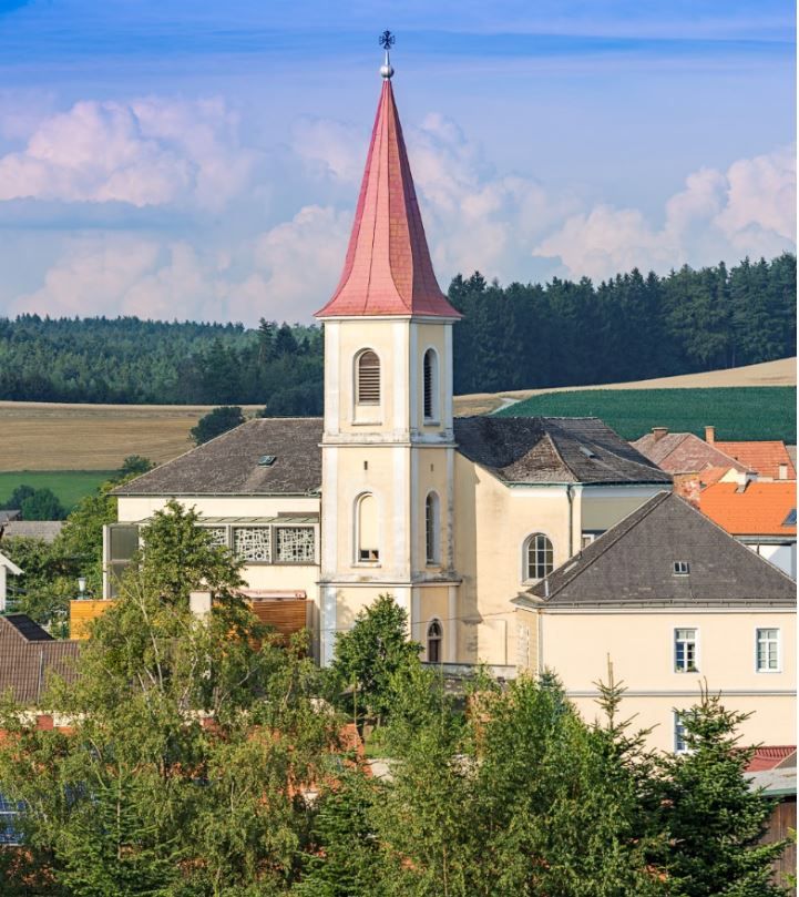Hochwolkersdorfi plébániatemplom piros, csúcsos toronytetővel és a környező tájjal.