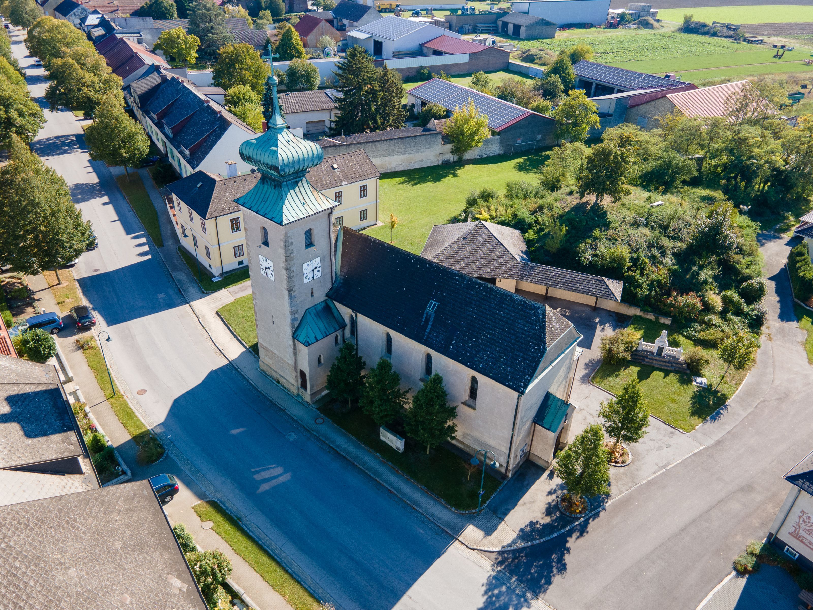 Légi felvétel a Weiden an der March településen álló templomról, tornyával, réz tetővel, valamint a környező házakkal és kertekkel.