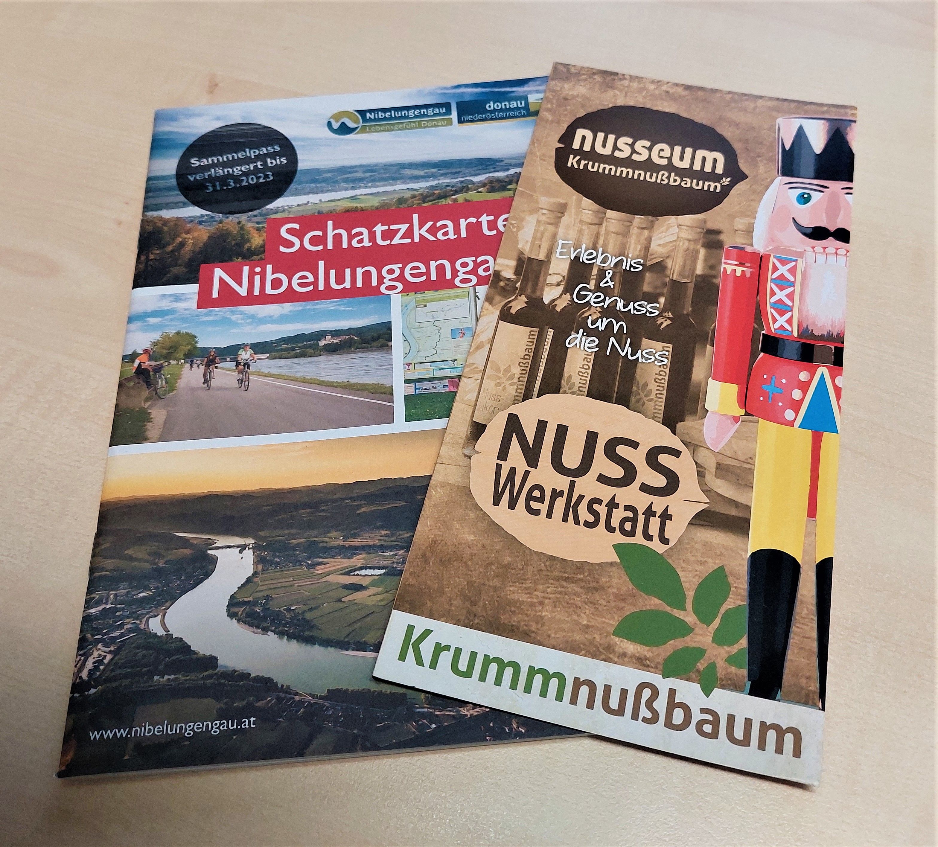 Két prospektus egy asztalon: egy a Nibelungengau kincses térképéről és egy a Nusseum Krummnußbaumról.