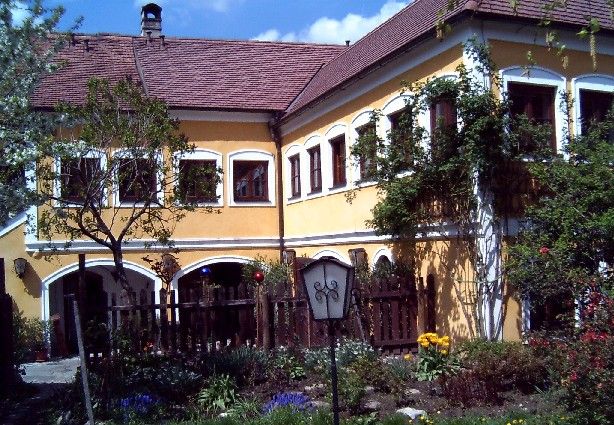 Sárga ház piros tetőcseréppel és kerttel az előtérben.