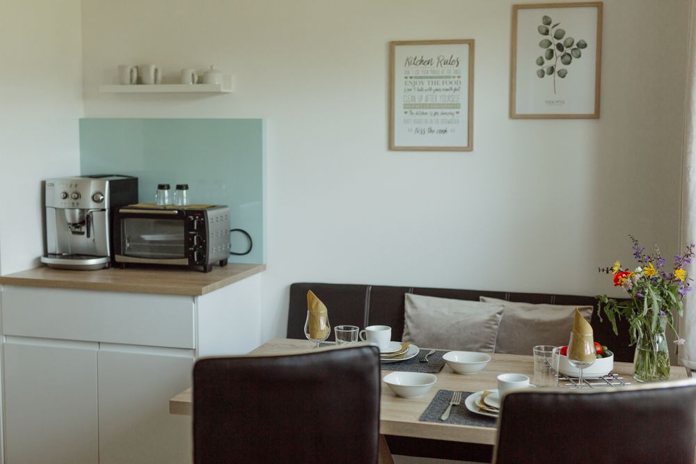 Kis konyha kávéfőzővel, sütővel, étkezőasztallal és virágokkal.