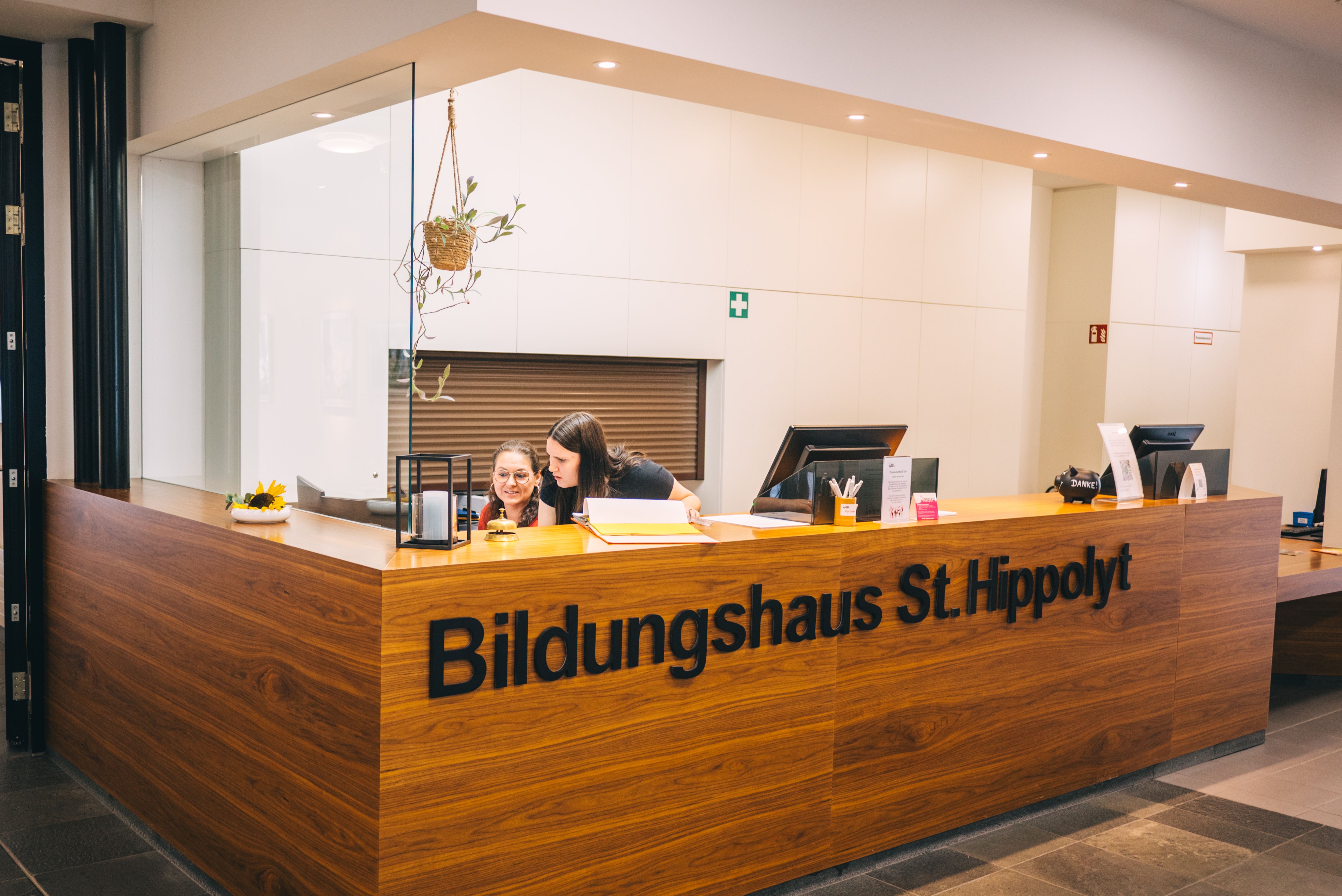 Recepció a Szent Hippolyt oktatási központban, két emberrel egy fapult mögött.