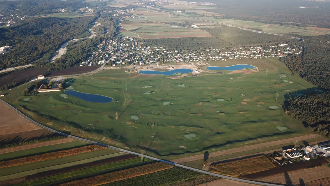 Légi felvétel egy golfpályáról, számos vízi veszéllyel és a szomszédos településről.