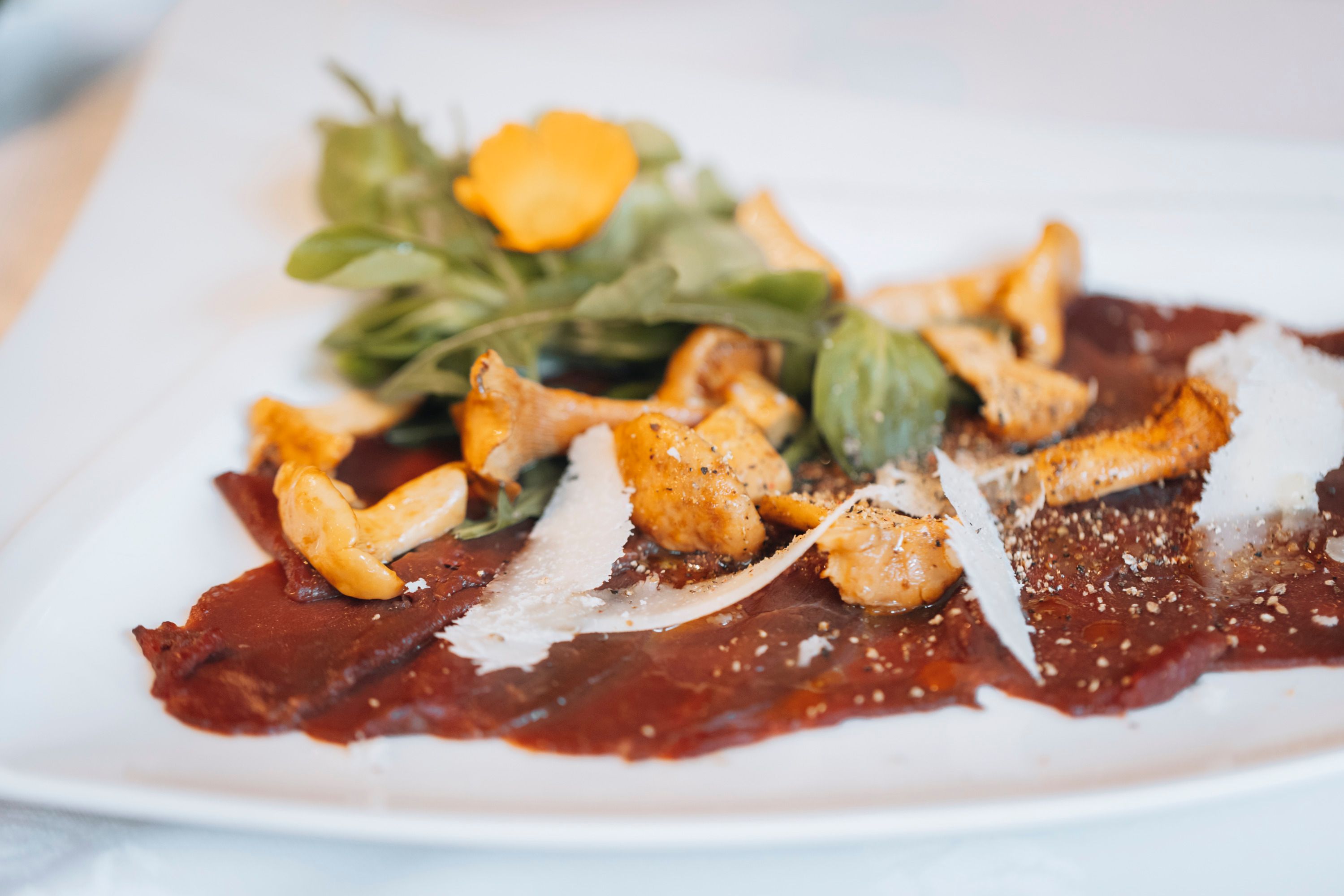 Carpaccio dámszarvasból, savanyított rókagombával és rukkolával fehér tányéron.