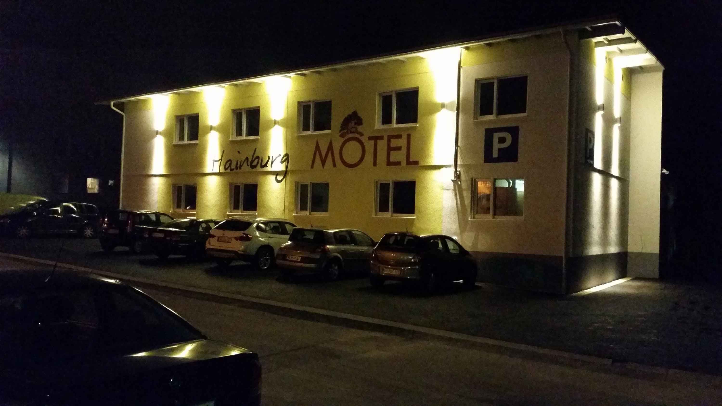 Éjszakai felvétel egy kivilágított motelről a "Hainburg Motel" felirattal és az előtte parkoló autókkal.