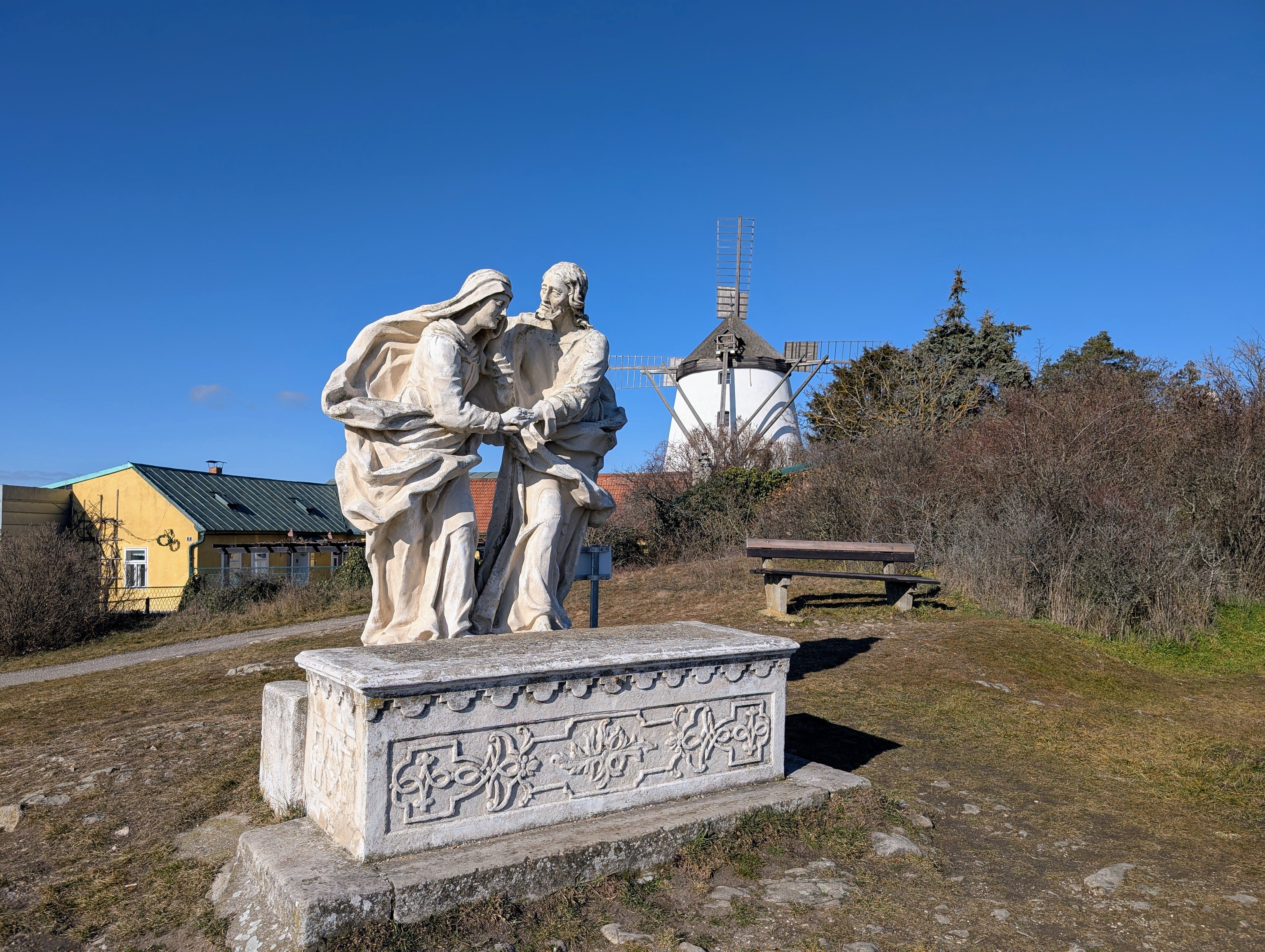 Kőszobor egy dombon, a háttérben szélmalom.